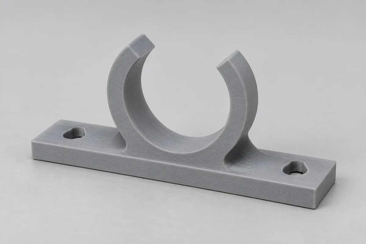 Grauer gedruckter Rohrclip für 22 mm mit Grundplatte und zwei Senkbohrungen vor hellgrauem Hintergrund