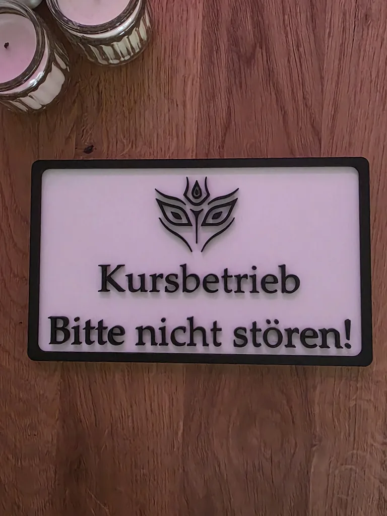 Door sign „Kursbetrieb, Bitte nicht stören!“ with a logo, white with a black frame, seen from the front on a wooden table