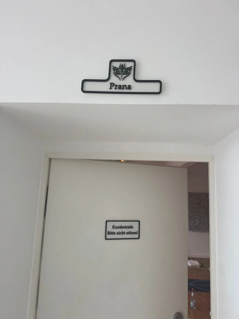 Printed room sign „Prana“ with a logo above a door and a door sign „Kursbetrieb: Bitte nicht stören!“ at the Shakti Yoga studio in Cologne